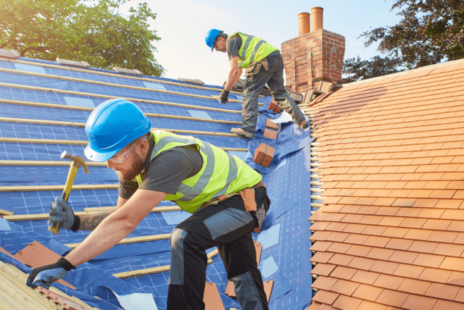 Skilled roofers in safety gear urgently installing new terracotta tiles on a steep roof, with a focus on quality and speed, indicative of emergency roofing services.