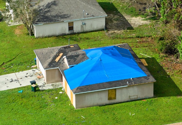 A man installing a tarp on a roof to provide temporary leak repair.