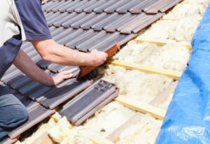 A person repairing a roof, using tools and shingles to patch up small holes.