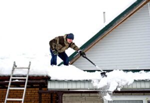 A man removes snow from the roof with the help of shovel