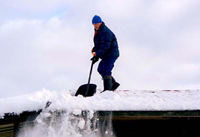 Man cleaning the roof from snow with a shovel