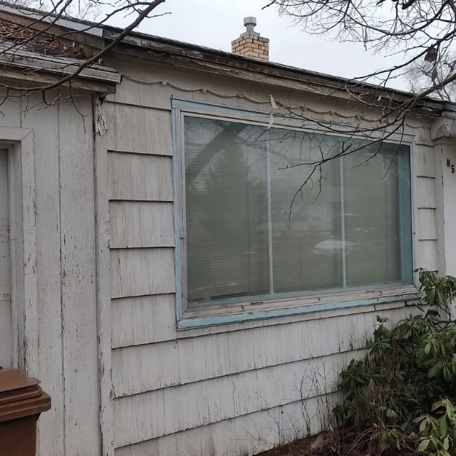 Exterior of an aged house with a large window showing signs of wear on the wood siding, indicative of window replacement needs in Spokane.