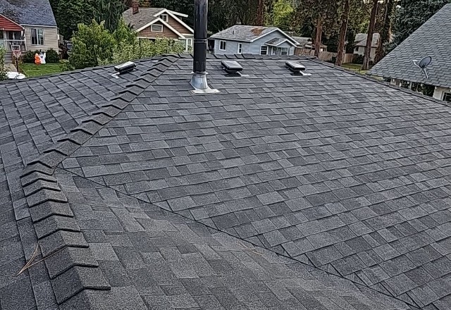 Freshly replaced asphalt shingle roof in Spokane Valley, with vent pipes and a chimney, highlighting quality roofing craftsmanship