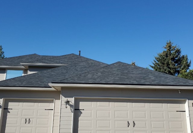 A close view of a shingle rooftop on a sunny day in Nine Mile Falls, WA, after a roof replacement or repair, with a clear blue sky backdrop