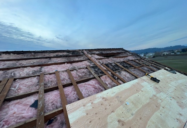 Before-phase of a roofing project showcasing exposed pink insulation between wooden beams, underlayment, and partial plywood cover, a project started by an insulation company in Spokane
