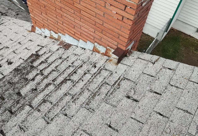 Worn-out asphalt shingles with missing granules near a chimney, suggesting the need for services from a roofing contractor in Spokane