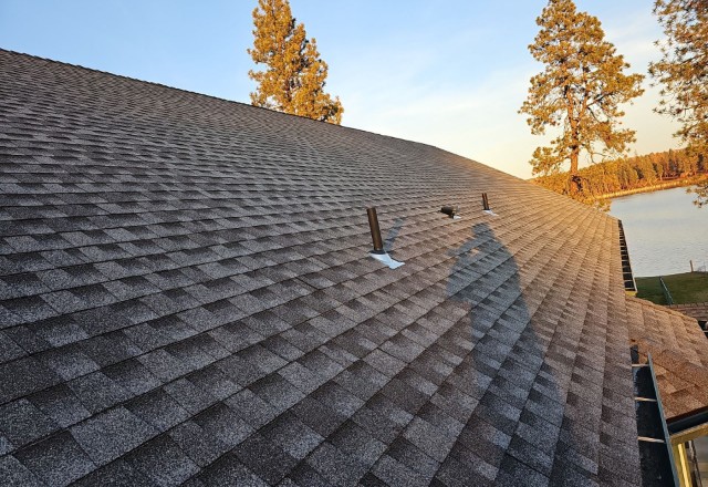 Sunset hues cast over a freshly replaced roof in Spokane Valley, highlighting the even shingle pattern and the roof's peak with a clear sky and treeline silhouette.