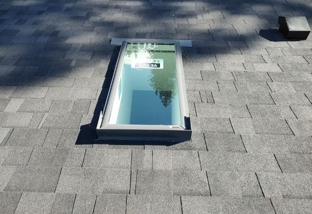 After replacement: A newly installed, pristine skylight on an asphalt shingle roof, showcasing the clear view through the clean glass.