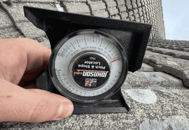 Hand holding a pitch gauge against a slate tile roof, a crucial tool for roof inspections to determine the slope, used by roofing companies in Spokane