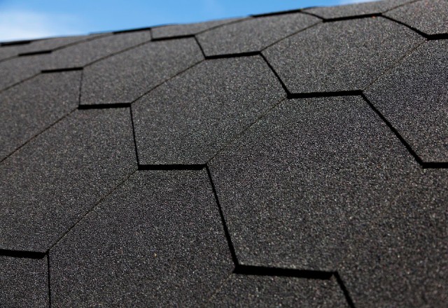 Detailed view of asphalt shingle roofing installation in Spokane, highlighting the overlapping pattern and texture of the dark shingles against a clear sky.