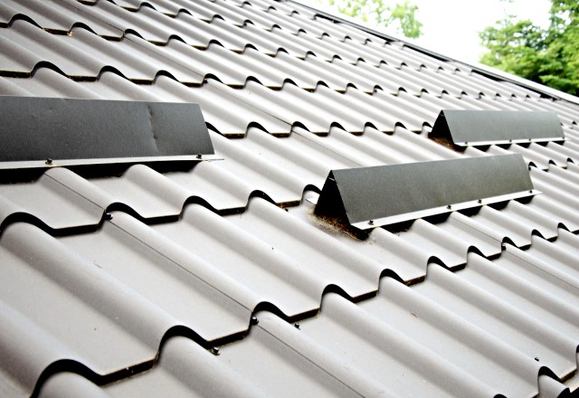 Sloped metal roofing installation in Spokane, with a focus on the wavy pattern of the grey metal sheets and the visible screws securing them against a cloudy sky