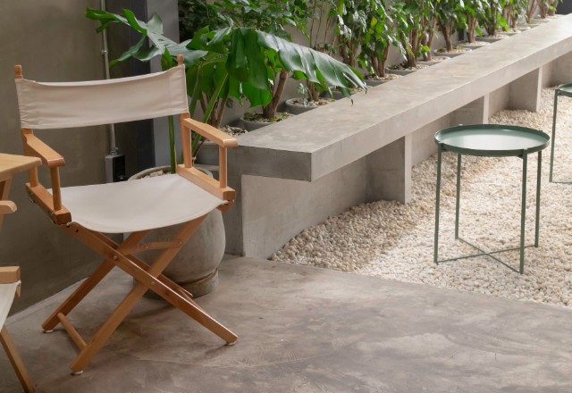 Modern outdoor seating area by a concrete company in Spokane, showing a stylish director's chair with a white canvas, a sleek green metal table, and a concrete bench adorned with greenery.