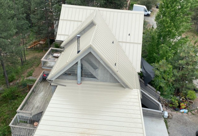 Elevated view of a home after a metal roof replacement, featuring a pristine white metal roof with clean lines and angles, surrounded by a lush wooded area