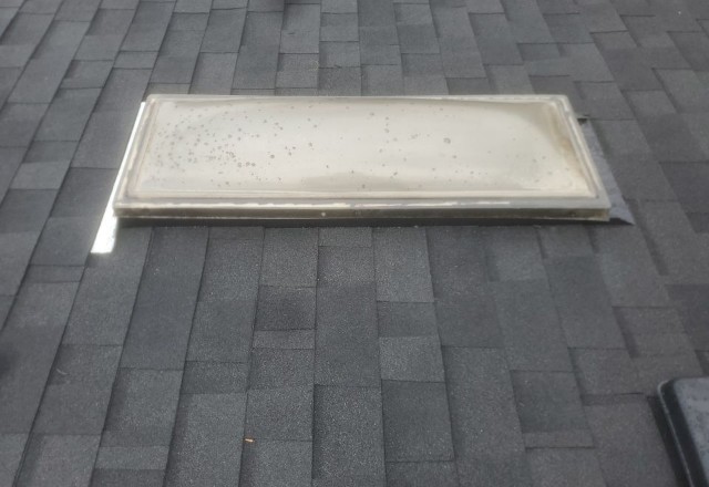 Before replacement: A worn and dirty skylight on an asphalt shingle roof, showing signs of aging and potential leakage.