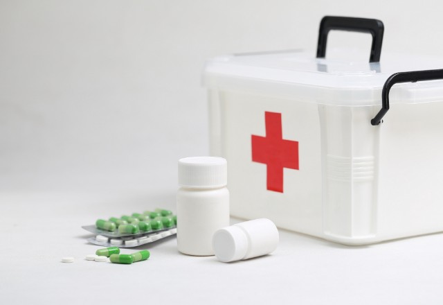 A white first aid box with a red cross, alongside spilled capsules and medicine bottles, representing preparedness to treat allergic reactions to hornet stings.