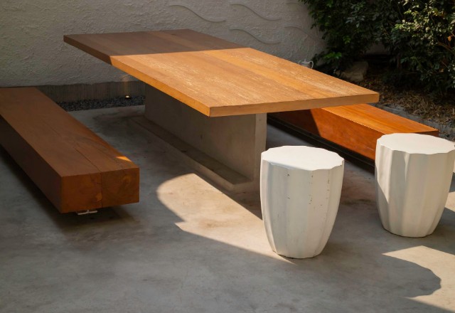 Custom-designed outdoor furniture on a concrete patio in Spokane, featuring a wooden table with a smooth finish and geometric concrete stools basking in the sunlight.