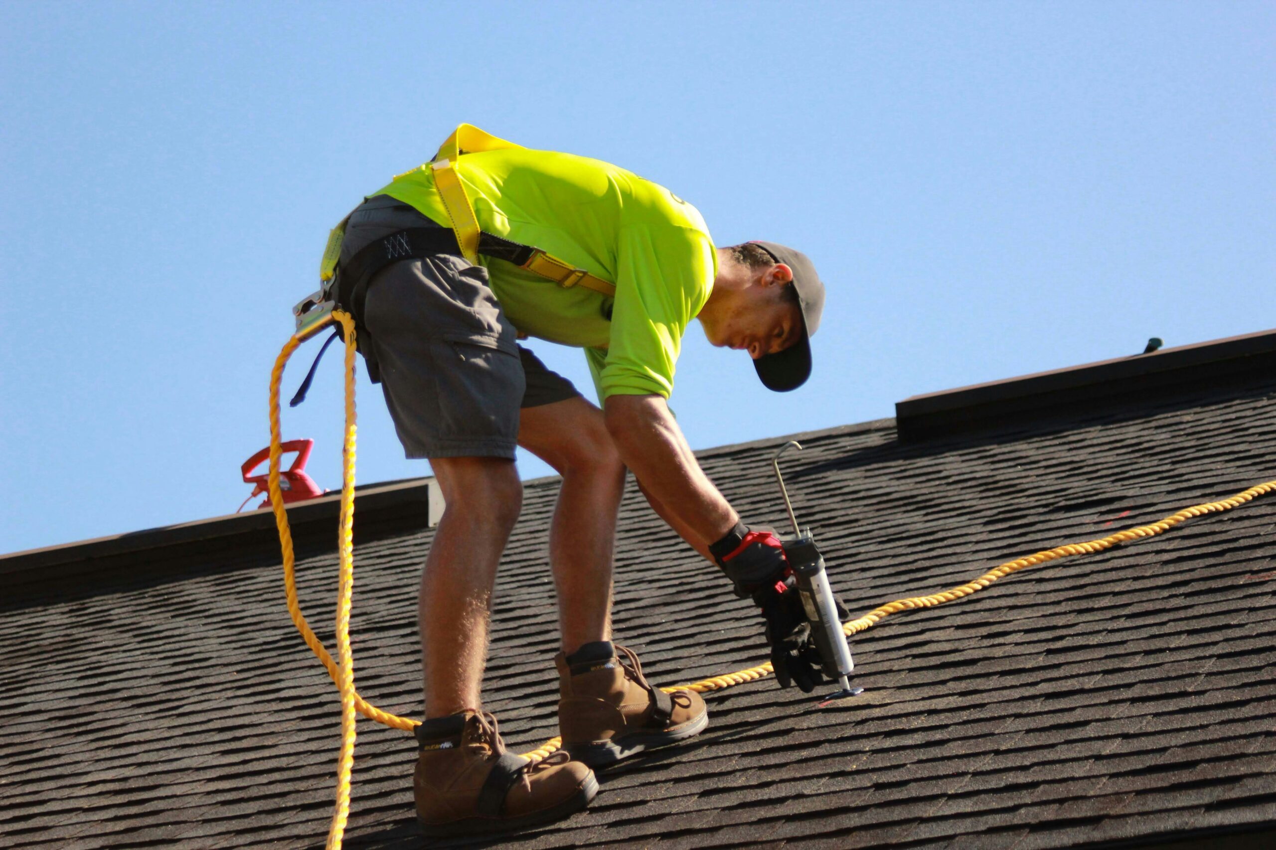 roofer from a local roofing company serving Newman Lake, WA secured with a safety, is installing shingles on a steep residential roof on a sunny day.