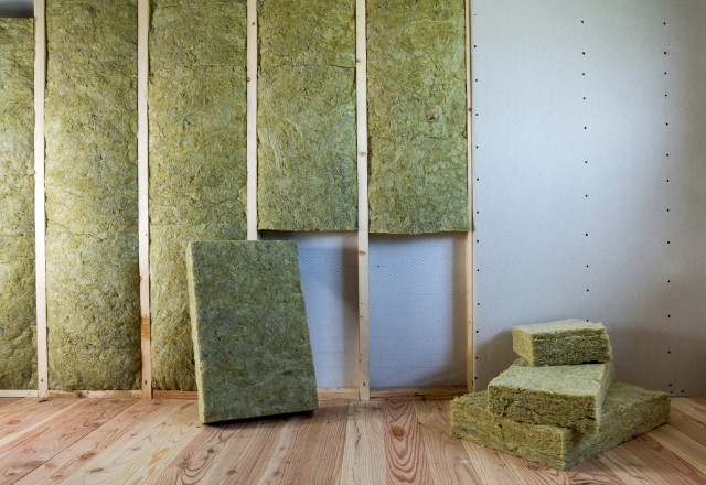 Neatly placed rockwool insulation pieces between the studs of an attic wall, with a stack of additional insulation pads on a wooden floor, ready for installation.