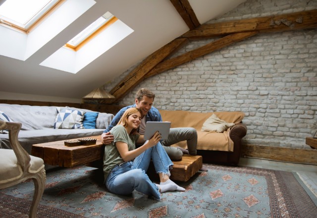 A happy couple enjoys a cozy moment in a comfortably insulated attic with rockwool insulation visible in the ceiling, enhancing the room's comfort and warmth.