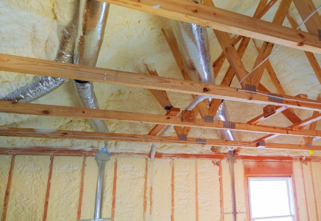 Newly installed heating system pipes amidst spray foam insulation on an attic ceiling, highlighting the durability concerns of how long does spray foam insulation last.