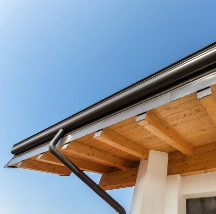 Underneath view of black seamless gutters installed on a wooden eave of an ecological house, a modern upgrade in residential roofing in Spokane