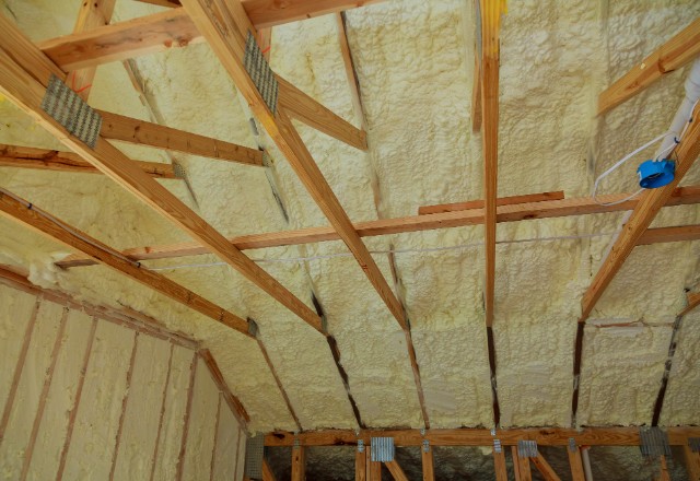 Interior view of a building's attic showing exposed wooden beams and sprayed foam insulation, a factor in discussing how long does spray foam insulation last