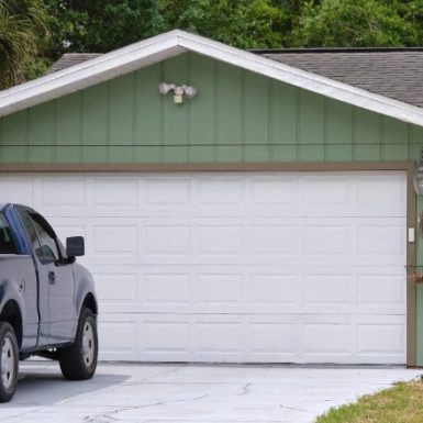 Green residential garage with white door, serviced by Spokane pole building contractors, with a blue truck parked in the driveway