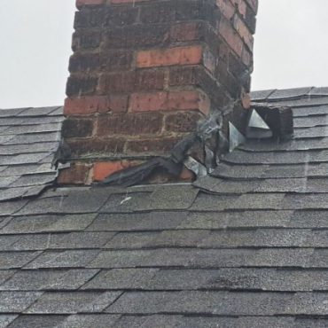 Worn asphalt shingle roof with a damaged chimney flashing, showing signs of deterioration and a gap exposing the roof structure