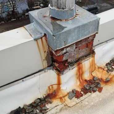 Rusted chimney flashing with orange rust stains dripping down on a flat white roof, signifying potential water ingress