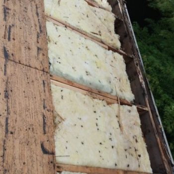 Partial installation of yellow fiberglass insulation on a wooden roof structure, depicting an intermediate step in an insulation replacement project.