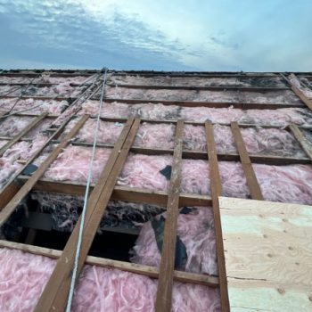 A before picture of roof insulation by an insulation contractor in Spokane, displaying pink fiberglass material and open wooden beams, indicating common insulation problems