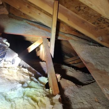 An attic space in Spokane showing insulation issues, with old fiberglass batts and a spotlight highlighting the area needing repair.