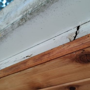 Close-up of a roof's edge showing a cracked and peeling white sealant above a wooden fascia board, suggesting water damage and the need for repair