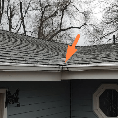 Close-up of a gutter with visible cracks on a shingled roof, pinpointing typical wear that requires attention from a Spokane gutter repair contractor