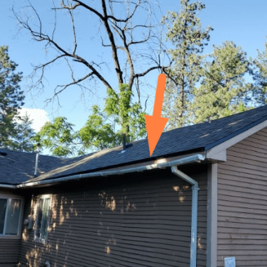 Exterior shot of a home with an uneven gutter system and downspout, with the surrounding trees suggesting the need for Spokane gutter repair contractor