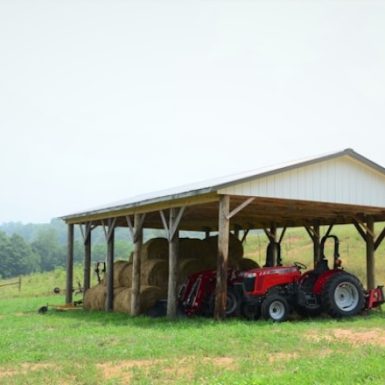 Functional open-sided pole shed by Spokane pole builders, housing hay bales and a red tractor, perfect for Spokane's agricultural storage needs.