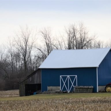 Sturdy blue pole barn in a fallow field, a testament to the durable construction by Spokane pole building contractors against a backdrop of bare trees